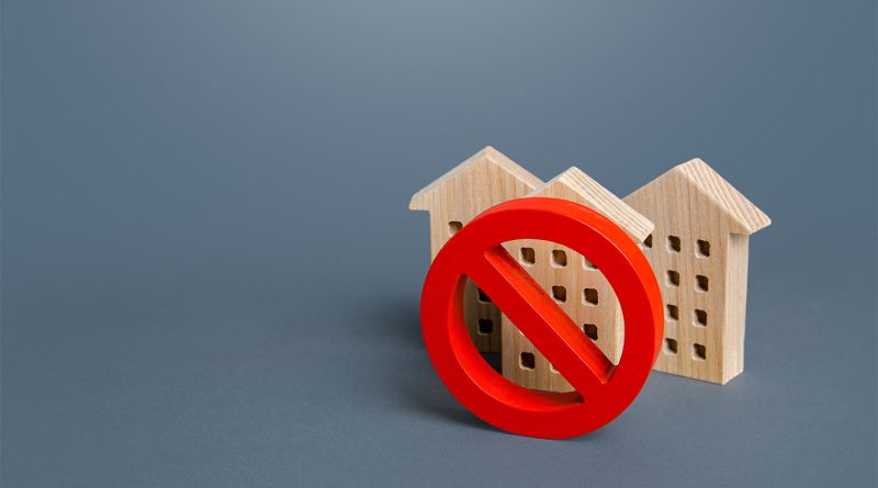 Image of some model houses sat on a surface with a red 'no entry' style circle sign in front of them to support construction shortages article