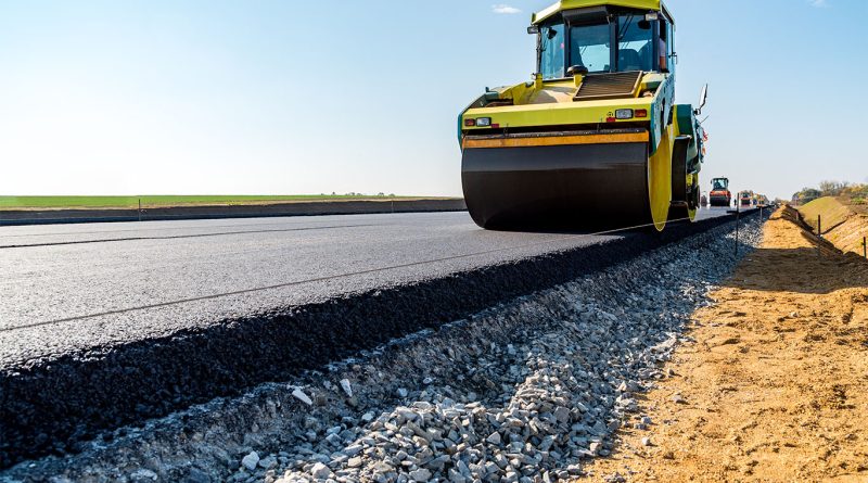 Image of a road with cement being rolled on top by a construction vehicle to support road construction article