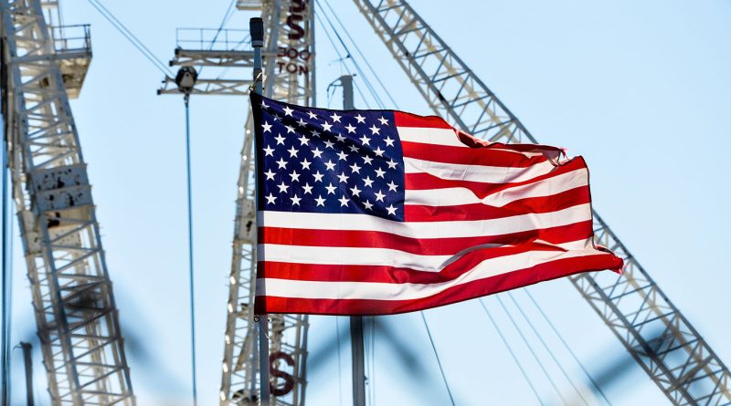 Image of the American flag in front of various different cranes and construction machinery to support US construction article