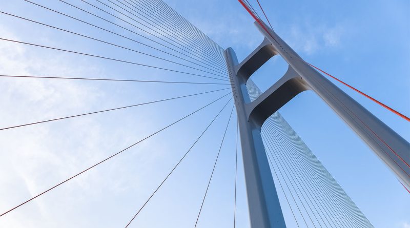 A close-up ground-up view of a cable bridge with blue skies behind it to support US Canada bridge article