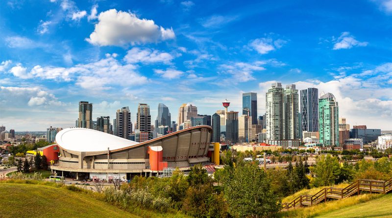 Panoramic image of Calgary downtown featuring the skyline, blue skies and a green field area