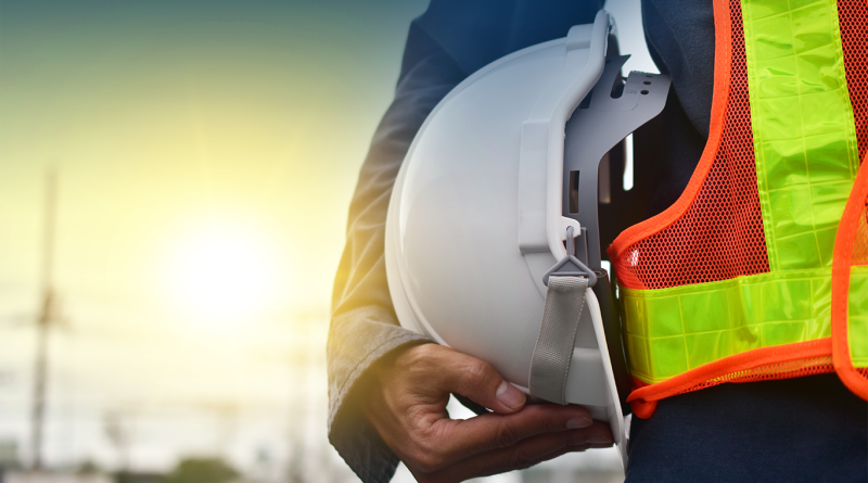 Close up image of a construction worker in a high-visibility vest, holding their hard hat next to them to support US construction article