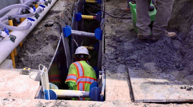 Construction worker in a safety vest working inside a trench supported by shoring systems, showcasing safety and structural stability in construction projects.