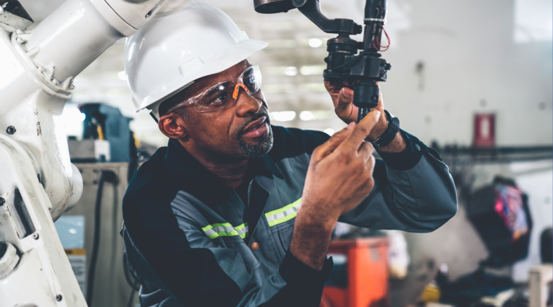 A worker in a hard hat and safety gear adjusting a robotic arm, showcasing robotics construction technology.