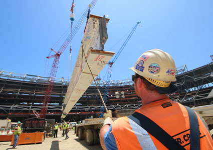 Steel I beam being raised by a crane in a stadium construction