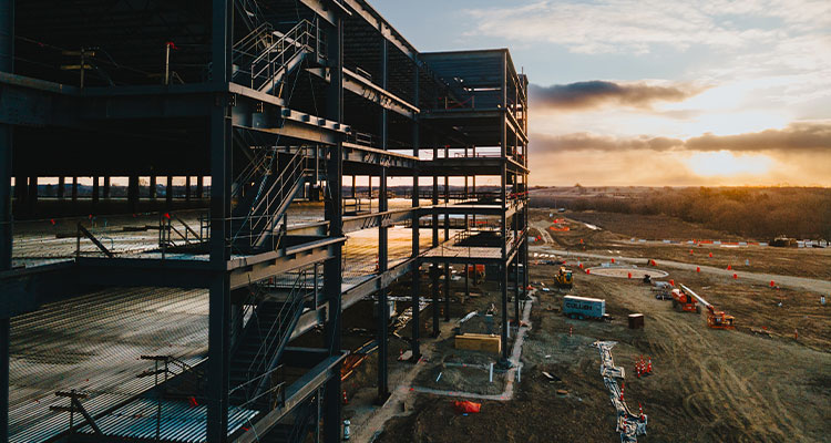 Committed to enhancing and innovating the construction industry, BZI® is setting new safety standards and accelerating project delivery Amazon Fulfillment Center under construction, likely depicting the steel structure of a large warehouse facility at sunset.