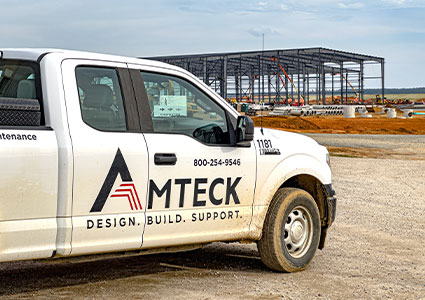 the side of a white Amtek pickup truck with a construction site in the background