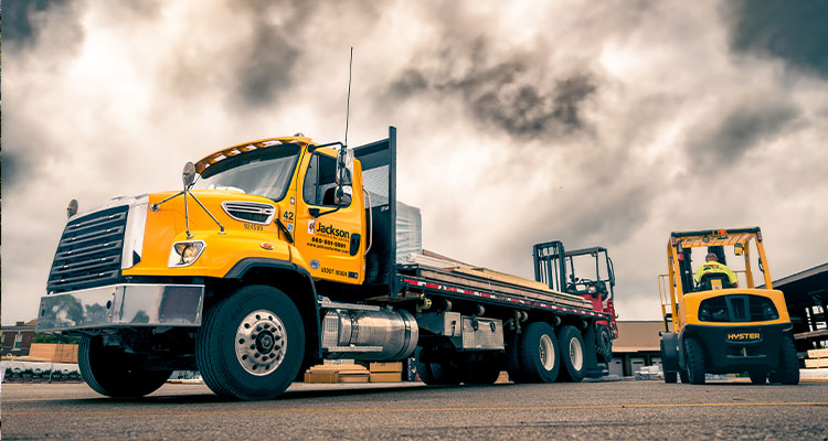 a bright yellow Jackson Lumber & Millwork commercial flatbed truck