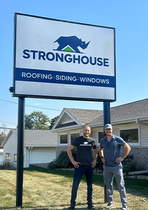 a large outdoor sign for Stronghouse, with two men standing in front of it.