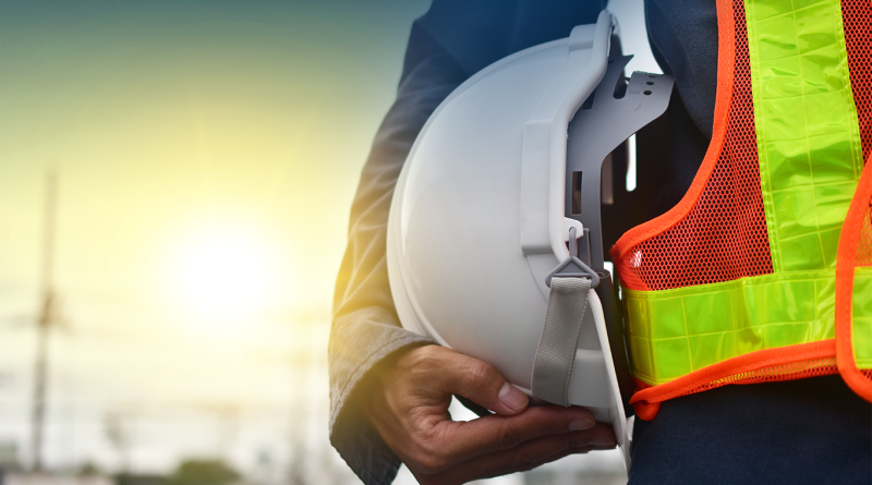 Construction worker holding a white hard hat while wearing a high visibility safety vest on a job site