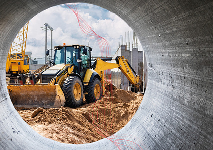  a yellow backhoe loader at a construction site, captured from a unique perspective through a large concrete pipe