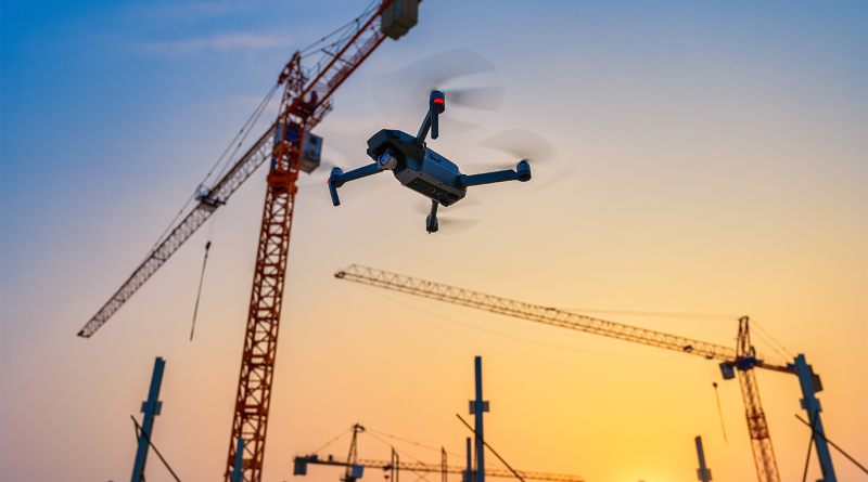 Construction drone flying above an active construction site with tower cranes and steel framework at sunset.