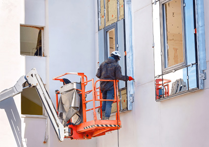  a worker in a Genie lift basket caulking or sealing the exterior window frame of a commercial building