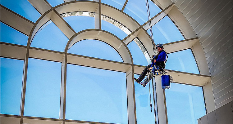 a professional window cleaner utilizing abseiling equipment (rope access) to clean large, high-rise windows