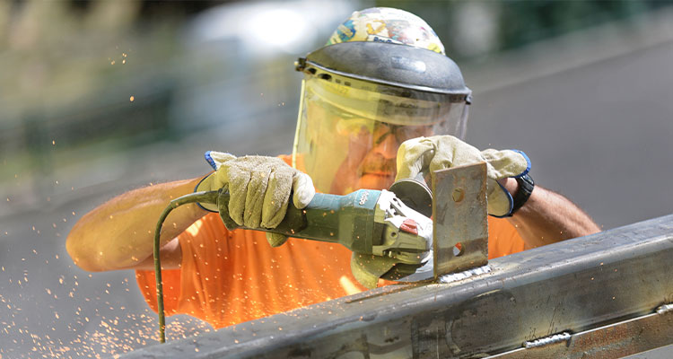 a worker using an angle grinder to grind or smooth a metal weld on a steel structure