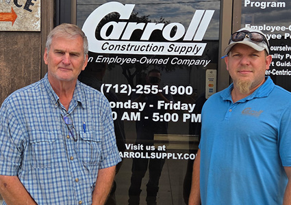 two men standing in front of a glass door displaying the logo and phone number for Carroll Construction Supply