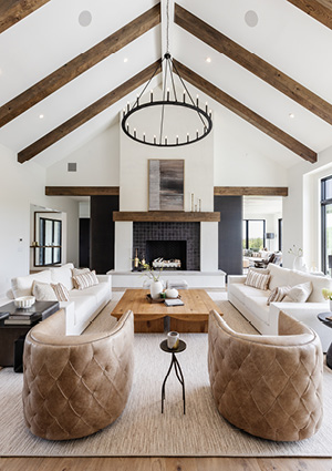 living room features a vaulted ceiling with exposed wood beams, a central fireplace, and tufted tan swivel chairs 